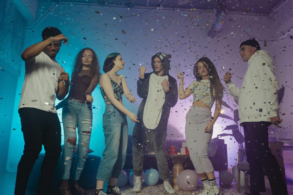 Un groupe de jeunes adultes divers dansant et s'amusant lors d'une fête en salle avec des confettis et des ballons.